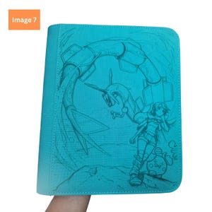 Puede incluir: Una carpeta de color turquesa brillante con una ilustraci&oacute;n de l&iacute;neas en azul cerceta que muestra una criatura serpentina, una figura humana y un peque&ntilde;o personaje redondo. La cubierta tiene una textura y esquinas redondeadas con cremallera.
