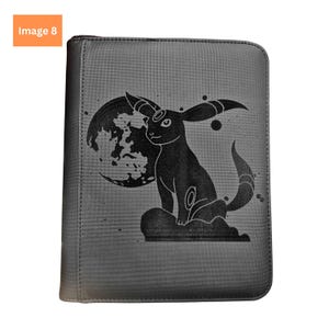 Puede incluir: Una carpeta rectangular negra con cremallera que presenta una ilustraci&oacute;n gr&aacute;fica oscura de un personaje Umbreon sentado frente a una luna grande. El dise&ntilde;o incluye peque&ntilde;os acentos circulares y una superficie texturizada en la cubierta.