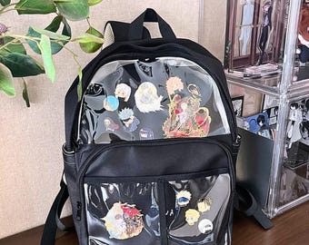 Może przedstawiać: Czarny plecak z przezrocznymi przednimi kieszeniami, w których znajdują się kolorowe emaliowane przypinki. Plecak ma górny uchwyt, regulowane paski i przednią kieszeń. Przypinki przedstawiają różne postacie w stylu anime w żywych kolorach.