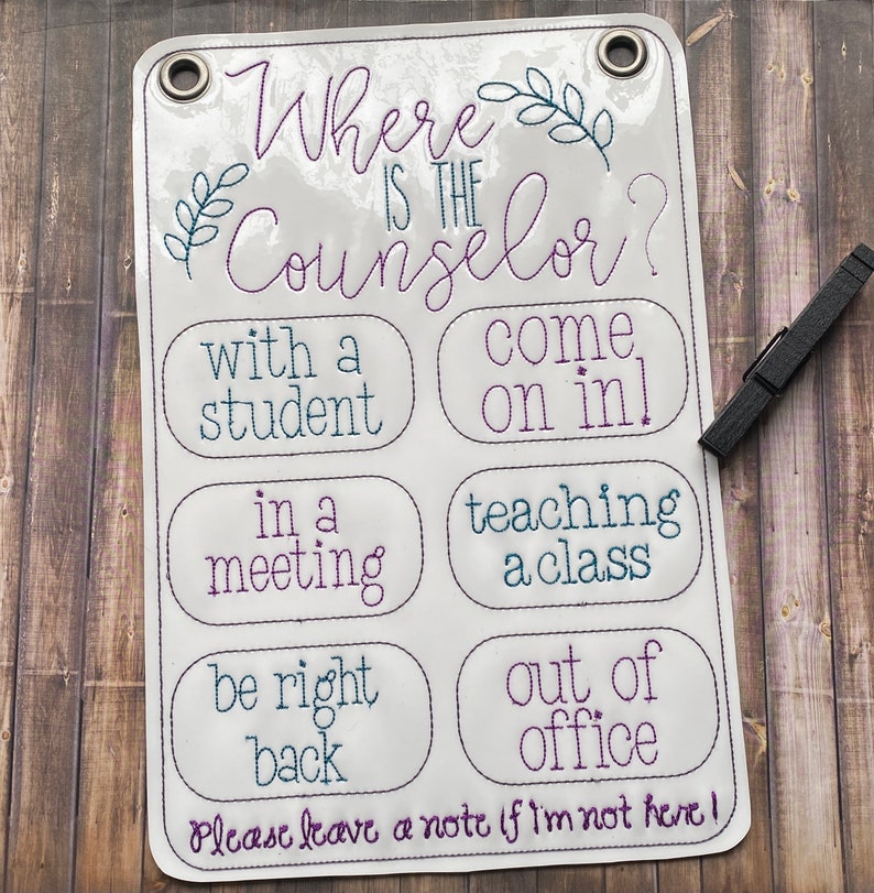 May include: White sign with the text "Where is the Counselor?" and a list of reasons why the counselor may be unavailable. The text is in a purple and teal font. The sign is hanging on a wooden surface.
