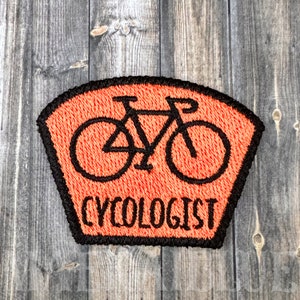 May include: Orange and black embroidered patch with a bicycle silhouette and the text "CYCOLOGIST".