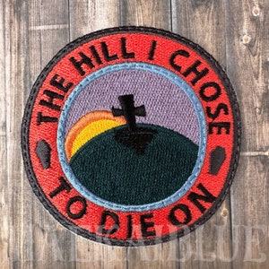 May include: Red embroidered patch with the text "The Hill I Chose To Die On" in a white circle with a black cross on a green hill with a yellow and orange sunset in the background.
