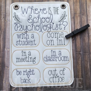May include: White sign with gold trim and black text that reads "Where is the School Psychologist?" with options to choose from: "with a student", "in a meeting", "be right back", "come on in!", "in a classroom", "out of office".