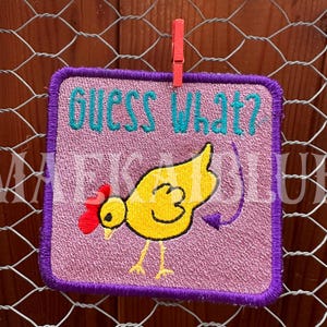 May include: Purple embroidered patch with a pink background. The patch features a yellow chick with a red comb and a blue tail feather. The text "Guess What?" is embroidered in blue on the patch.