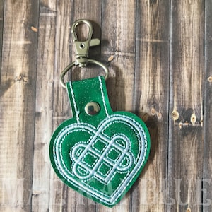May include: Green heart-shaped leather keychain with a silver metal clasp and a white Celtic knot design.