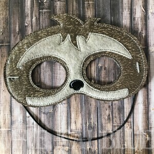 May include: Brown and white felt sloth mask with black elastic band. The mask has two eye holes and a black felt nose.