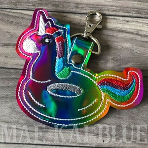 May include: A rainbow iridescent keychain featuring a unicorn shaped inflatable pool float. The unicorn has a white horn, a rainbow mane, and a rainbow tail.