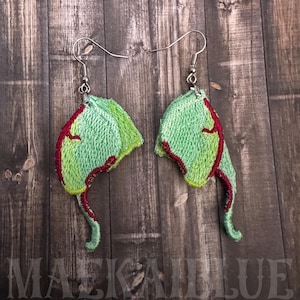 May include: A pair of handmade embroidered earrings. Each earring features a light green, leaf-shaped design with red and yellow accents. The earrings are suspended from silver-colored fish hook ear wires. The text "MAEKAIBLUE" is visible at the bottom.