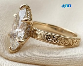May include: A gold ring featuring a large marquise-cut center stone held by prongs. The band is decorated with intricate engraved scrollwork patterns and small pavé-set stones along the setting. The text DK JEWELS is visible in blue.