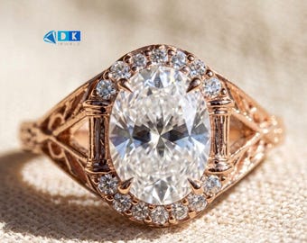 May include: A rose gold ring featuring a large oval-cut center stone surrounded by a halo of small round stones. The band displays intricate filigree metalwork on the sides. The logo DK JEWELS is visible in the upper left corner of the image.