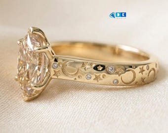 Pode incluir: Um anel de ouro com uma grande pedra central de corte marquise fixada por garras. A banda é gravada com motivos celestiais, incluindo luas crescentes e estrelas, acentuados com pequenos diamantes redondos incrustados. O texto DK JEWELS é visível.