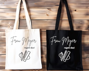 Könnte beinhalten: Zwei Stofftaschen, eine weiße und eine schwarze, mit dem Text "Frau Meyer regelt das!" und einer Grafik mit einem Bleistift, einem Lineal und einem Radiergummi.
