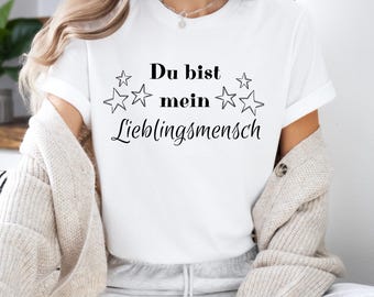 Op de afbeelding: Wit T-shirt met zwarte tekst die "Du bist mein Lieblingsmensch" zegt met sterren rond de tekst.
