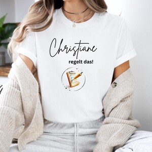Può includere: Maglietta bianca con testo nero che dice "Christiane regelt das!" e una grafica di una clipboard con una lista di controllo e una matita.