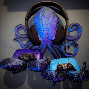 May include: A purple and blue PlayStation 5 controller is held by a 3D printed octopus wall mount. The octopus is holding a pair of black headphones. The octopus is painted in a blue and purple color scheme.