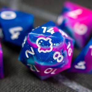 Può includere: Un set di dadi blu e rosa con numeri bianchi e un simbolo di fantasma su un dado. I dadi hanno un motivo a spirale, simile a una galassia.