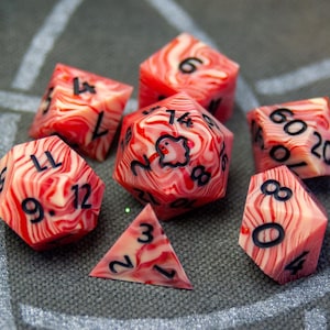 May include: Set of seven red and white swirl dice with black numbers. The dice are a d4, d6, d8, d10, d12, and d20. One of the d6 dice has a ghost icon instead of a number.