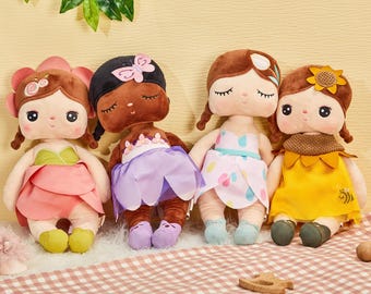 May include: Four plush dolls with different outfits and hair colours. The dolls are wearing dresses with floral patterns and have closed eyes.
