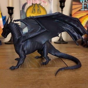 May include: A dark blue dragon figurine with wings outstretched. The dragon has a long tail and detailed scales. The figurine is made of plastic and is about 10 inches long.