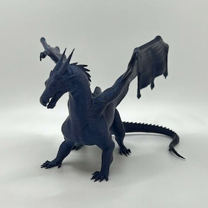 May include: A dark blue 3D printed dragon figurine with wings outstretched. The dragon has a textured, scaly body and a long tail.