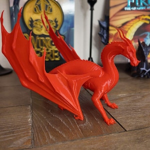 May include: A bright orange 3D printed dragon figurine with outstretched wings. The dragon has a long, slender neck and a detailed head with a pointed snout.