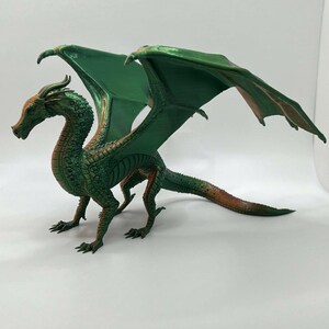 May include: A green and orange dragon figurine with outstretched wings. The dragon has a long tail and detailed scales.