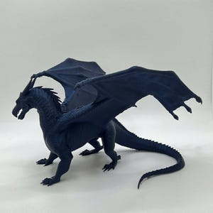 May include: A dark blue 3D printed dragon figurine with outstretched wings and a long tail. The dragon is posed in a standing position with its head turned to the side.