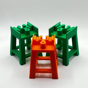 May include: Three small, colorful, plastic stools. Two are green and one is orange. The stools have a simple design with a square base and four legs.
