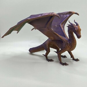 May include: A 3D printed dragon figurine with purple and brown wings and a textured, brown body. The dragon is standing on a white surface.