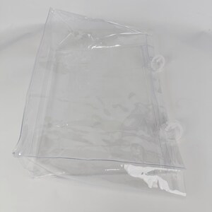 K&ouml;nnte beinhalten: Eine transparente, rechteckige Plastikt&uuml;te mit abgerundeten Ecken und einer Naht entlang der Kanten. Die T&uuml;te hat zwei transparente, kreisf&ouml;rmige Verschl&uuml;sse auf einer Seite. Die T&uuml;te ist transparent und scheint leer zu sein.