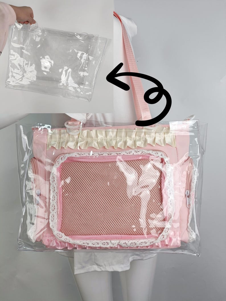 K&ouml;nnte beinhalten: Eine rosa Haustiertasche mit einer transparenten Kunststoffh&uuml;lle. Die Tasche hat ein Netzfenster, Spitzenbesatz und einen rosa Schultergurt. Eine separate transparente Plastikt&uuml;te ist ebenfalls sichtbar.