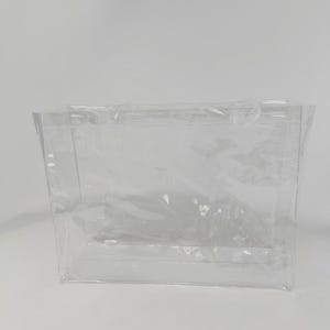 K&ouml;nnte beinhalten: Eine transparente Tragetasche mit zwei Griffen. Die Tasche besteht aus einem flexiblen, durchsichtigen Material und hat eine rechteckige Form. Die Tasche ist leer und steht vor einem wei&szlig;en Hintergrund.