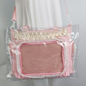 K&ouml;nnte beinhalten: Rosa Haustiertragetasche mit einer transparenten Kunststoffau&szlig;enschicht. Die Tasche hat ein Netzfenster, Spitzenbesatz und eine ger&uuml;schte Oberseite. Sie verf&uuml;gt &uuml;ber einen Schultergurt und zwei Seitentaschen mit Rei&szlig;verschl&uuml;ssen. Ideal f&uuml;r kleine Haustiere.