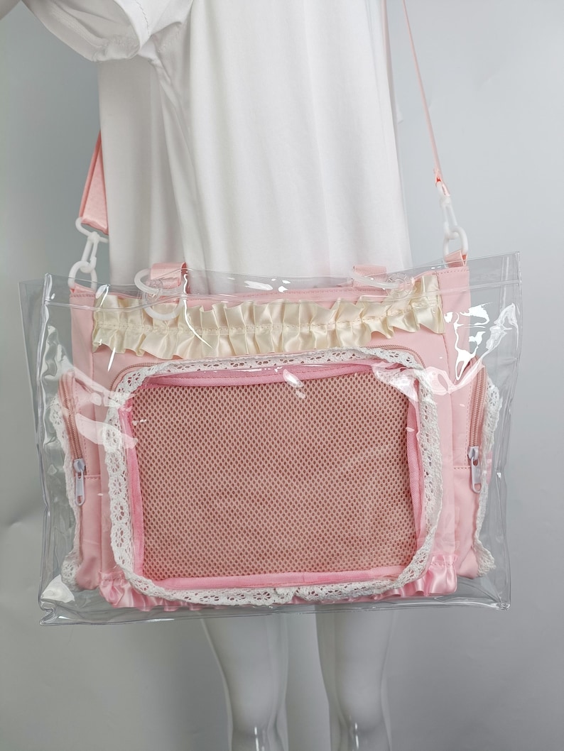 K&ouml;nnte beinhalten: Rosa Haustiertragetasche mit einer transparenten Kunststoffau&szlig;enschicht. Die Tasche hat ein Netzfenster, Spitzenbesatz und eine ger&uuml;schte Oberseite. Sie verf&uuml;gt &uuml;ber einen Schultergurt und zwei Seitentaschen mit Rei&szlig;verschl&uuml;ssen. Ideal f&uuml;r kleine Haustiere.