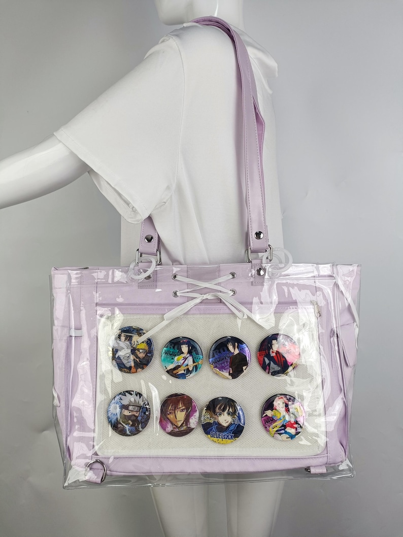 K&ouml;nnte beinhalten: Eine lavendelfarbene Tragetasche mit einem transparenten Frontpanel, das acht farbenfrohe Charakterpins zeigt. Die Tasche hat einen passenden lavendelfarbenen Riemen und silberfarbene Hardware. Die Tasche besteht aus einem klaren, transparenten Material.