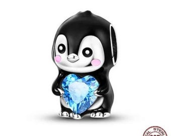 May include: A black and white penguin charm holding a blue heart-shaped gem. The penguin has pink cheeks and a silver base. The charm is made of sterling silver and has a 925 stamp.