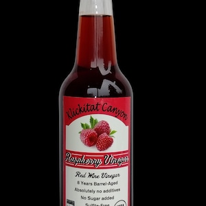 Puede incluir: Una botella de vidrio de vinagre de frambuesa Klickitat Canyon, un vinagre de vino tinto añejado durante 8 años. La botella está etiquetada con el nombre de la marca, el nombre del producto y detalles sobre el vinagre, incluyendo que está añejado en barrica, no tiene aditivos y es sin sulfitos. La botella es de 375 ml y tiene un sello USDA Organic.