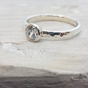 K&ouml;nnte beinhalten: Ein silberner Ring mit einem geh&auml;mmerten Band und einem klaren ovalen Edelstein.