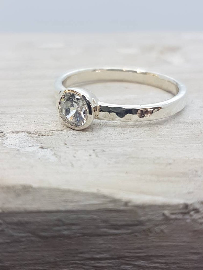 K&ouml;nnte beinhalten: Ein silberner Ring mit einem geh&auml;mmerten Band und einem klaren ovalen Edelstein.