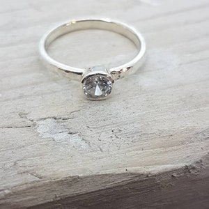 K&ouml;nnte beinhalten: Ein silberner Ring mit einem geh&auml;mmerten Band und einem klaren, runden Edelstein.
