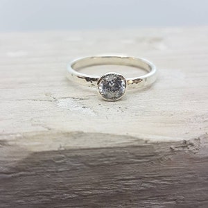 K&ouml;nnte beinhalten: Ein silberner Ring mit einem geh&auml;mmerten Band und einem runden, klaren Edelstein.