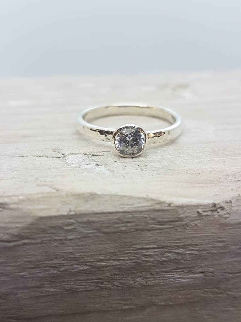 K&ouml;nnte beinhalten: Ein silberner Ring mit einem geh&auml;mmerten Band und einem runden, klaren Edelstein.