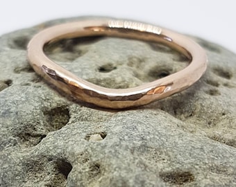 Könnte beinhalten: Ein gehämmerter Roségold-Bandring mit leicht gebogener Form. Der Ring liegt auf einem strukturierten grauen Stein.
