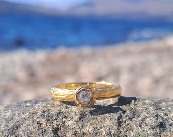 May include: A gold ring with a textured band and a single round diamond set in a bezel setting.