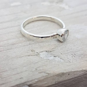 K&ouml;nnte beinhalten: Ein silberner Ring mit einem geh&auml;mmerten Band und einem gefassten, klaren Edelstein.