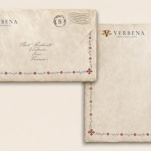 Könnte beinhalten: Ein cremefarbener Umschlag und ein passender Briefbogen mit einer dekorativen Bordüre aus kleinen roten Blumen und grauen Ranken. Beide Artikel zeigen den Text Verbena Poste Restante mit einem V-Logo. Der Umschlag enthält einen Poststempel.