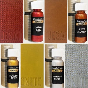 Puede incluir: Una colección de pinturas decorativas Jesmonite en varios colores, incluyendo Rojo Lava, Naranja Quemado, Miel Dorada y Plata Medianoche. Cada botella se muestra con una muestra de color correspondiente y el nombre de la marca.