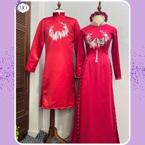 May include: Two red traditional outfits. The long-sleeved garments feature mandarin collars and white floral embroidery. The dress has a high collar and a row of pearls down the side. A matching floral headpiece is also visible.
