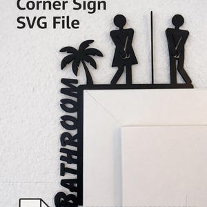 Può includere: Cartello angolare nero per bagno degli ospiti, con sagome di uomo e donna, una palma e la parola "Bathroom". File SVG digitale per taglio laser.