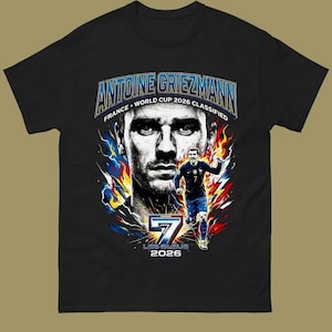 Może przedstawiać: Czarny t-shirt z grafiką Antoine'a Griezmanna, francuskiego piłkarza. Projekt zawiera portret, biegnącą postać oraz tekst "ANTOINE GRIEZMANN FRANCE WORLD CUP 2026 CLASSIFIED" i "7 LES BLEUS 2026".